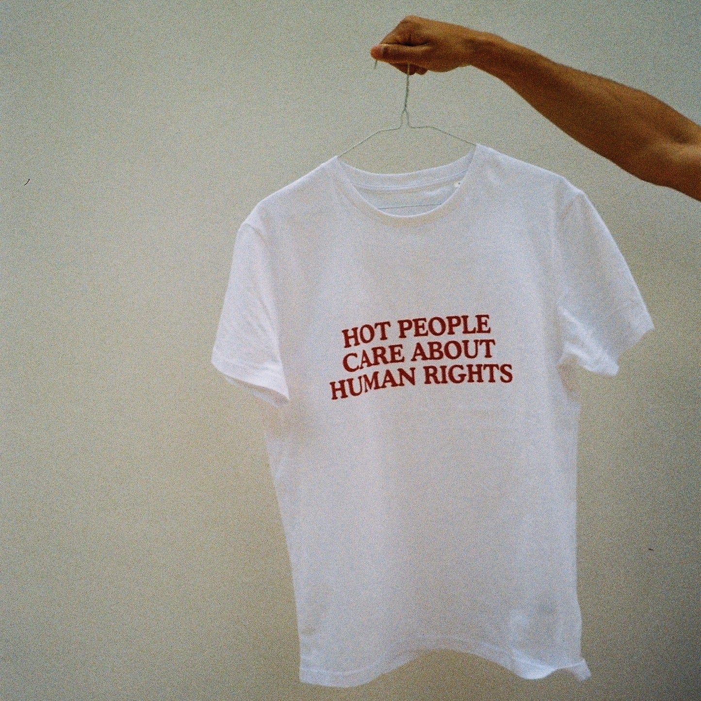 White t-shirt with red text held by a person against a light background