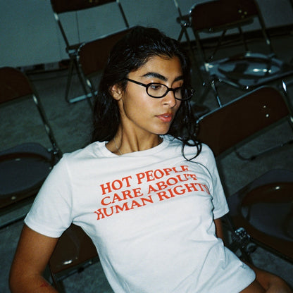 Person wearing a white t-shirt with red text in a room with chairs.