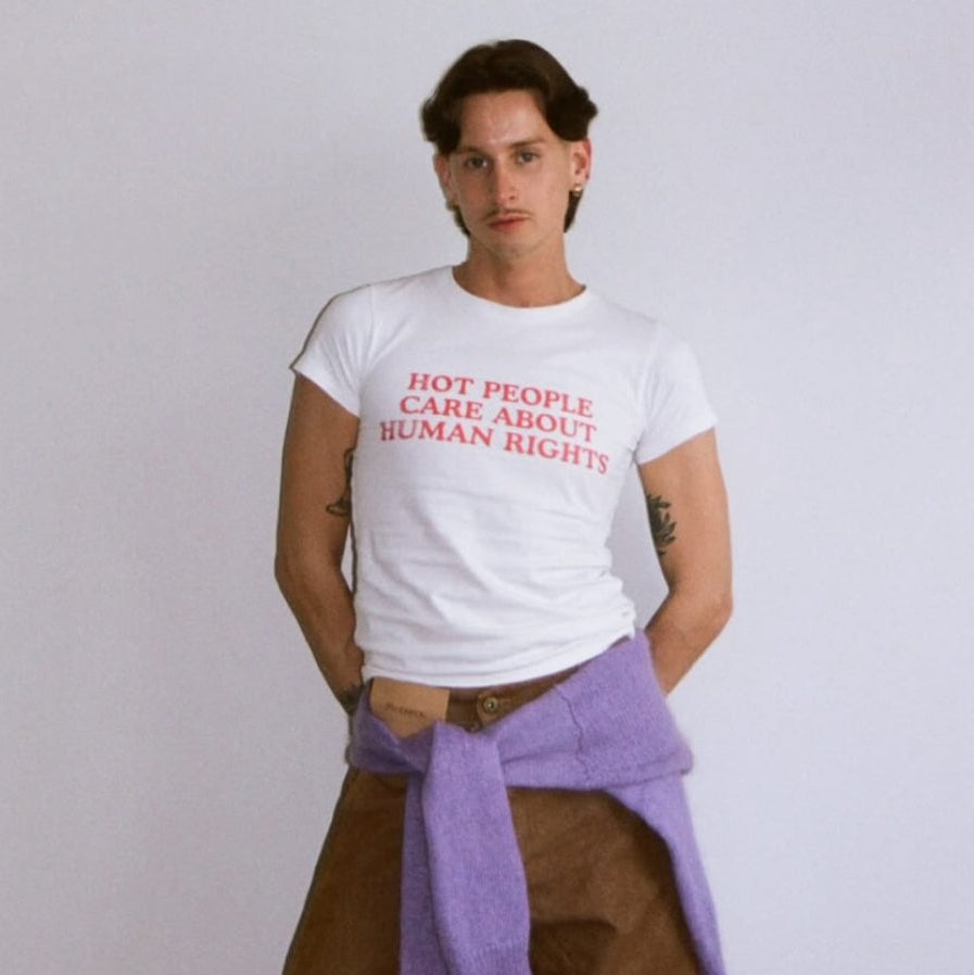 Person wearing a white t-shirt with red text and brown pants with a purple towel over one shoulder on a plain background