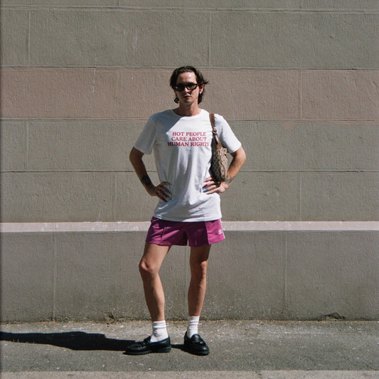 Person wearing a white t-shirt with text and pink shorts standing against a gray wall.